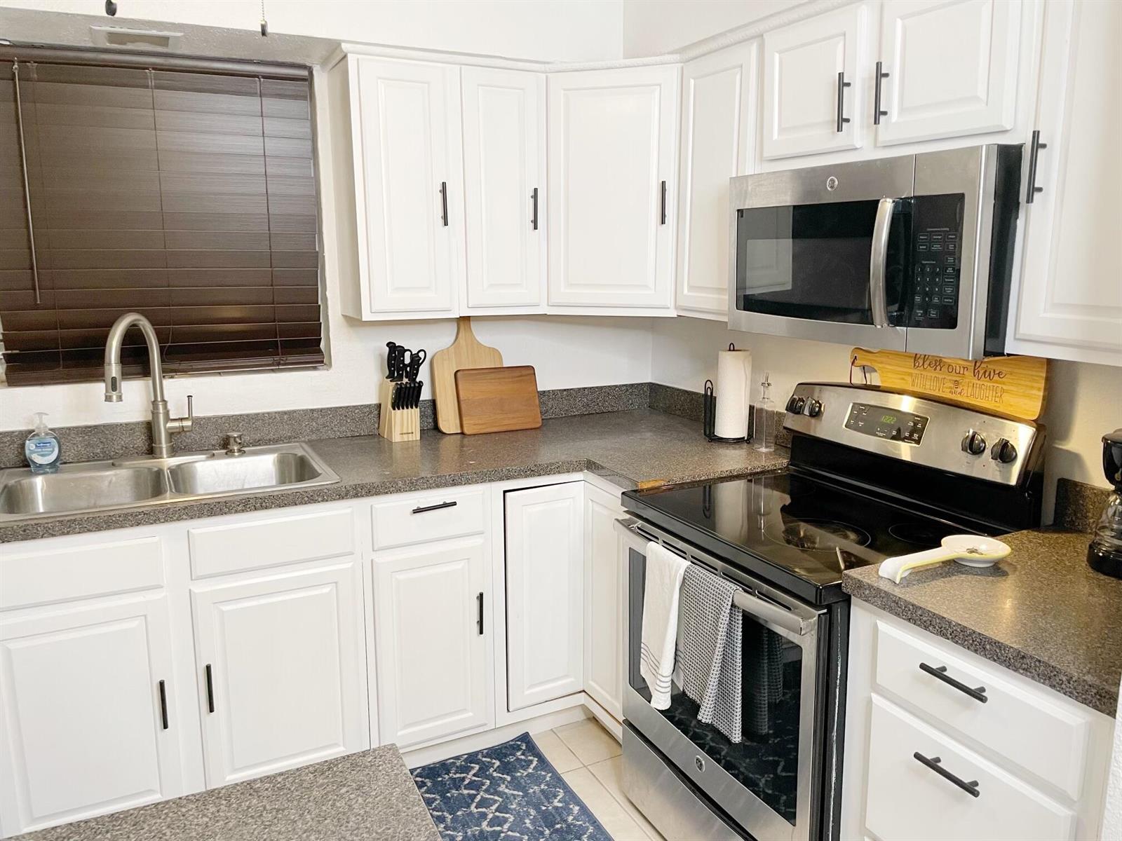 A kitchen features white cabinets, dark granite countertops, and stainless steel appliances — 1067 SW 3rd Street, Hallandale Beach FL 33009, HALLANDALE BEACH, FL