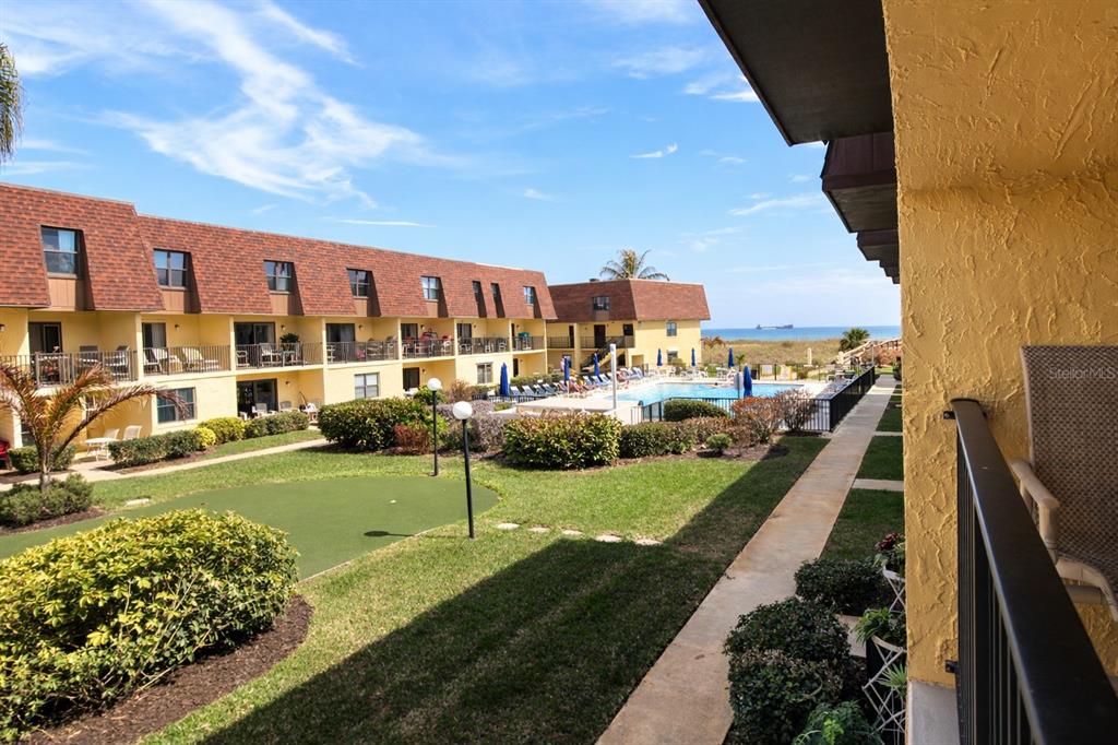 A view from a balcony overlooking a courtyard, swimming pool, and the ocean beyond — 5200 OCEAN BEACH BOULEVARD UNIT 213, COCOA BEACH, FL