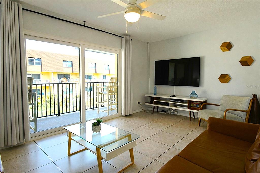 A living room features tile flooring, a glass coffee table, a television, and a balcony — 5200 OCEAN BEACH BOULEVARD UNIT 213, COCOA BEACH, FL