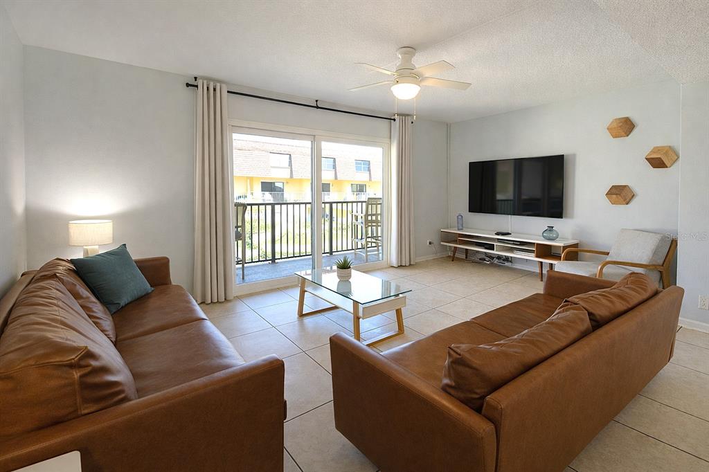 A living room features two brown leather sofas, a glass coffee table, and a television — 5200 OCEAN BEACH BOULEVARD UNIT 213, COCOA BEACH, FL