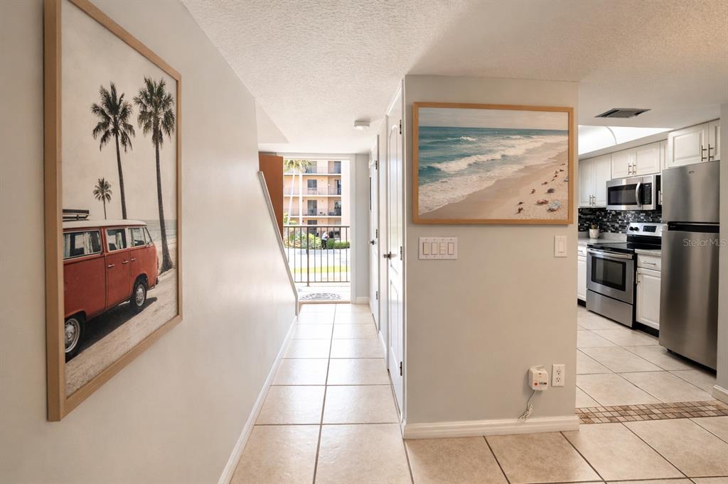 A hallway with tiled floors leads to a balcony, with a kitchen visible on the right — 5200 OCEAN BEACH BOULEVARD UNIT 213, COCOA BEACH, FL