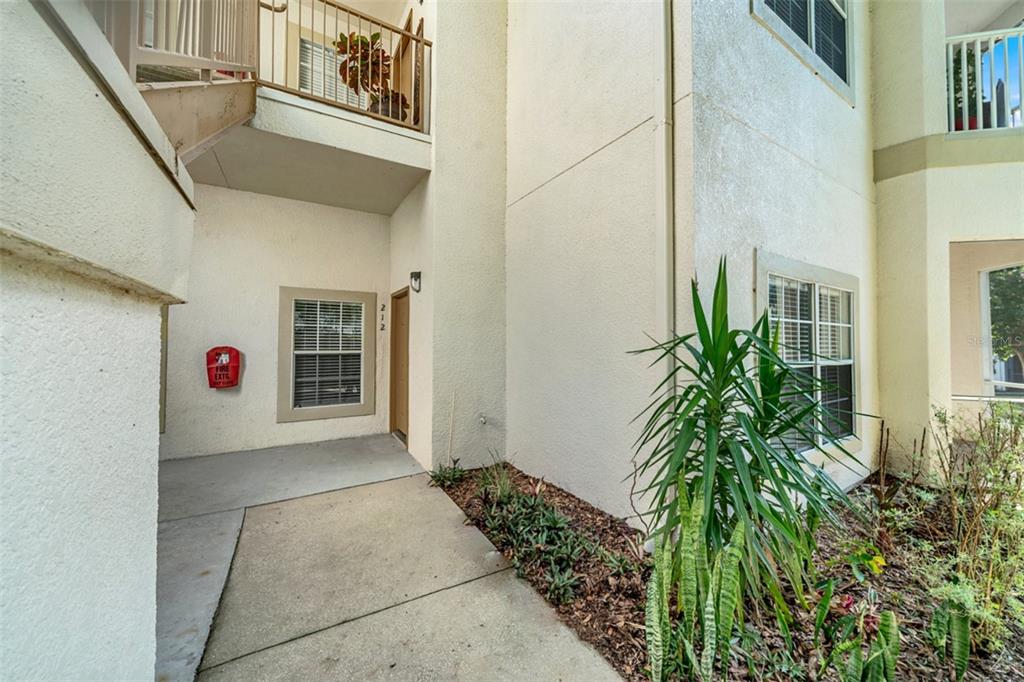 An exterior view of a ground-floor apartment entrance with a concrete walkway and landscaping — 970 N SPRING GARDEN AVENUE UNIT 212, DELAND, FL