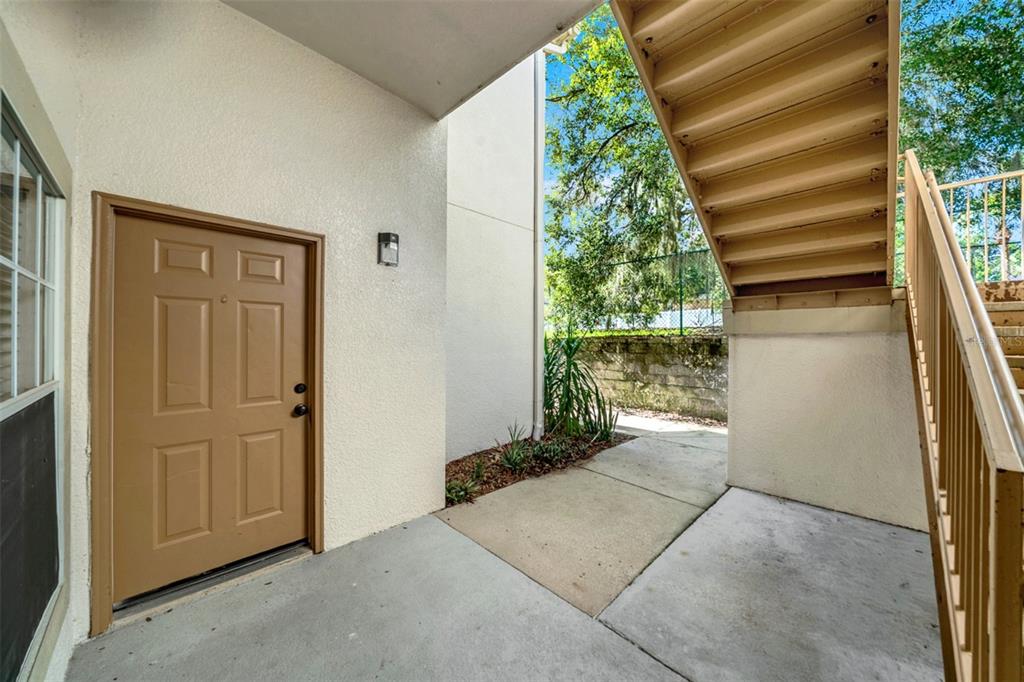 A tan exterior door sits on a concrete patio next to an outdoor staircase — 970 N SPRING GARDEN AVENUE UNIT 212, DELAND, FL
