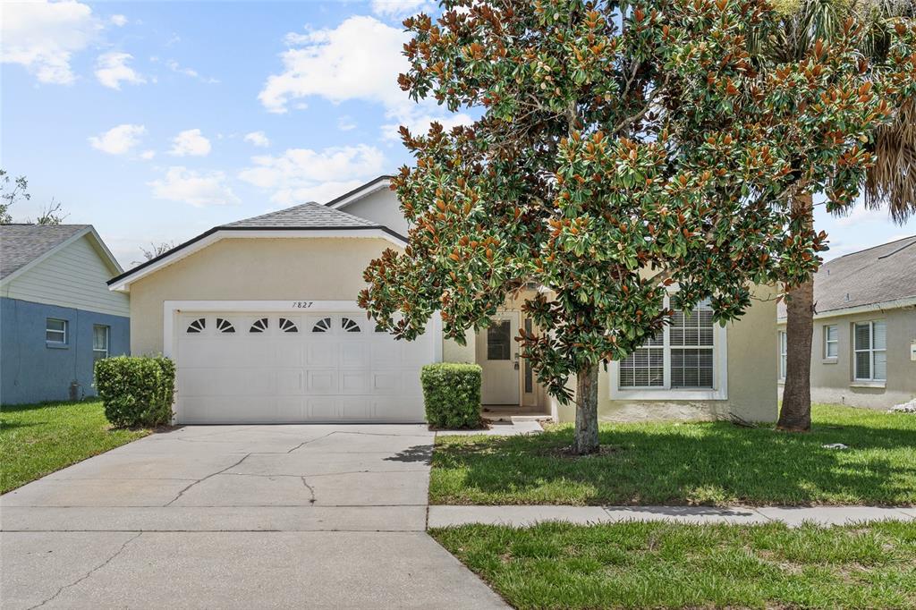 A single-story house with a two-car garage, a large tree, and a concrete driveway — 7827 MYRTLE OAK LANE, KISSIMMEE, FL
