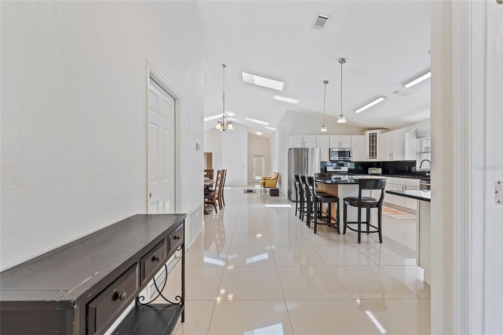 A bright, open-concept kitchen and dining area features white cabinetry, tile flooring, and vaulted ceilings — 7827 MYRTLE OAK LANE, KISSIMMEE, FL
