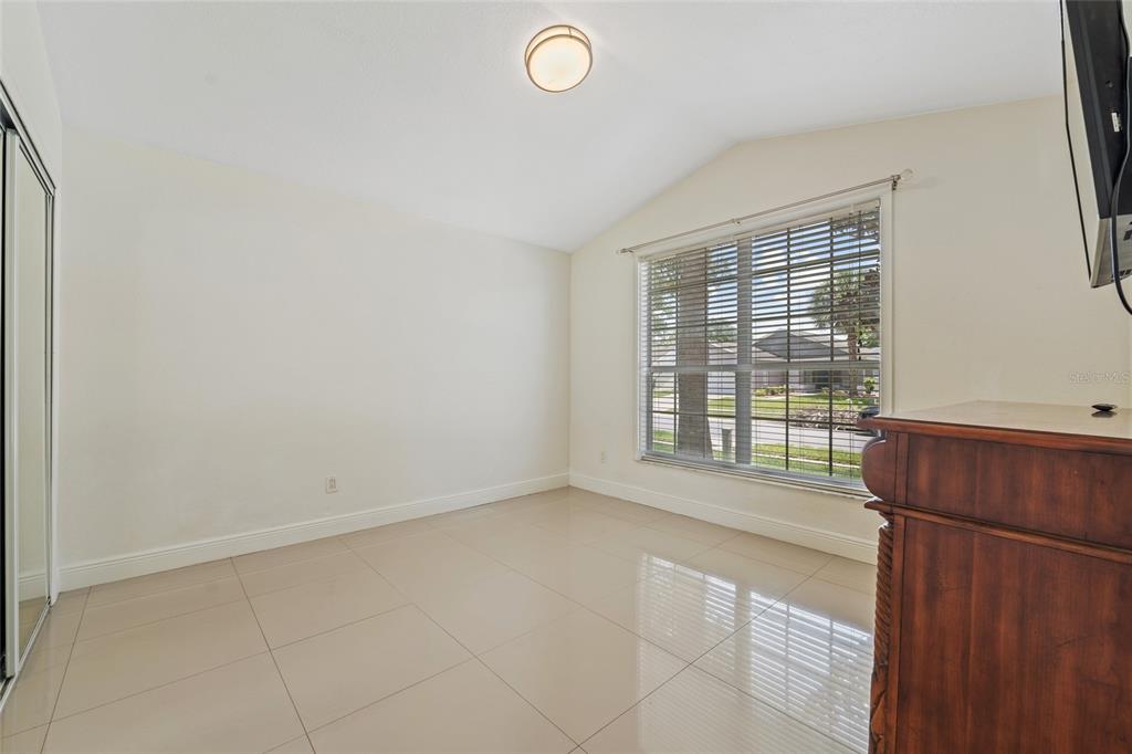 An empty room with light-colored tile flooring, a vaulted ceiling, and a large window — 7827 MYRTLE OAK LANE, KISSIMMEE, FL