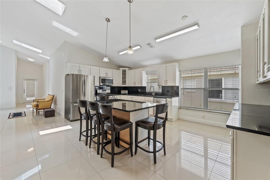 A modern kitchen features white cabinets, black countertops, a central island, and glossy tile flooring — 7827 MYRTLE OAK LANE, KISSIMMEE, FL