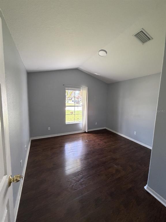 An empty bedroom features light gray walls, dark wood-look flooring, and a vaulted ceiling — 3035 BUCKEYE POINTE DRIVE, WINTER HAVEN, FL