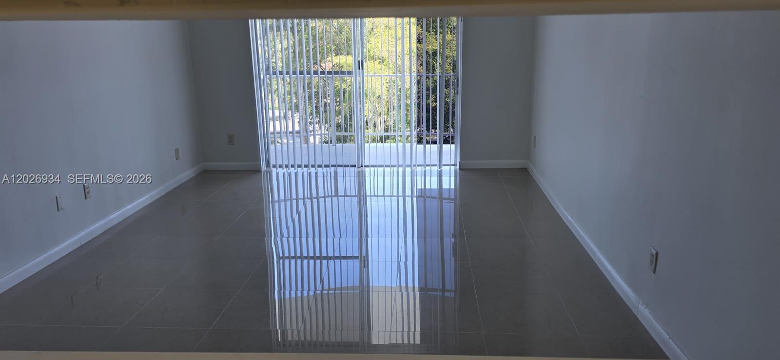 An empty room features large, glossy gray floor tiles and vertical blinds over a sliding door — 492 NW 165th St Rd # 511, Miami FL 33169, MIAMI, FL