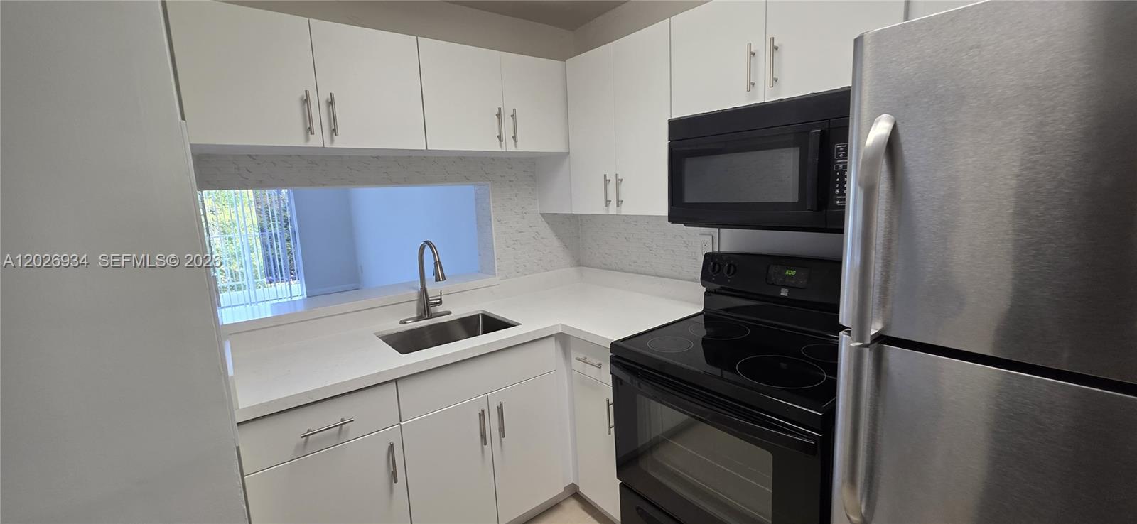 A kitchen features white cabinets, stainless steel appliances, and a pass-through window above the sink — 492 NW 165th St Rd # 511, Miami FL 33169, MIAMI, FL