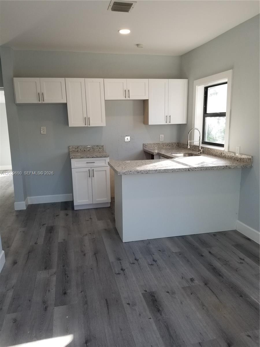A kitchen features white cabinets, granite countertops, and gray wood-look flooring — 1756 NW 94th St, Miami FL 33147, MIAMI, FL