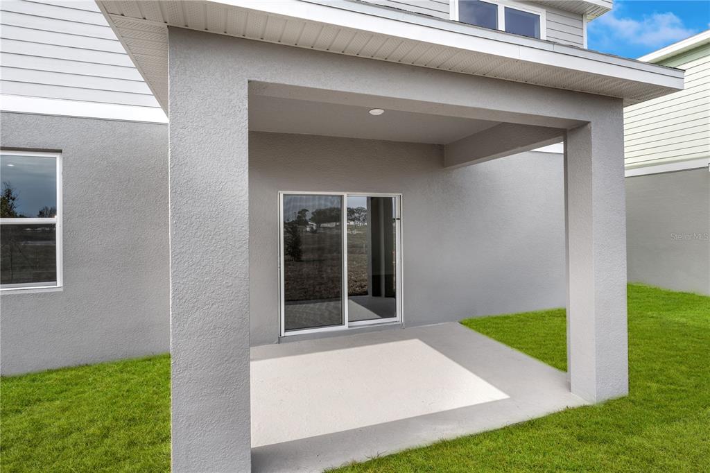 A covered concrete patio with a sliding glass door sits against a gray stucco house — 995 CONNOLLY LANE, PALM BAY, FL