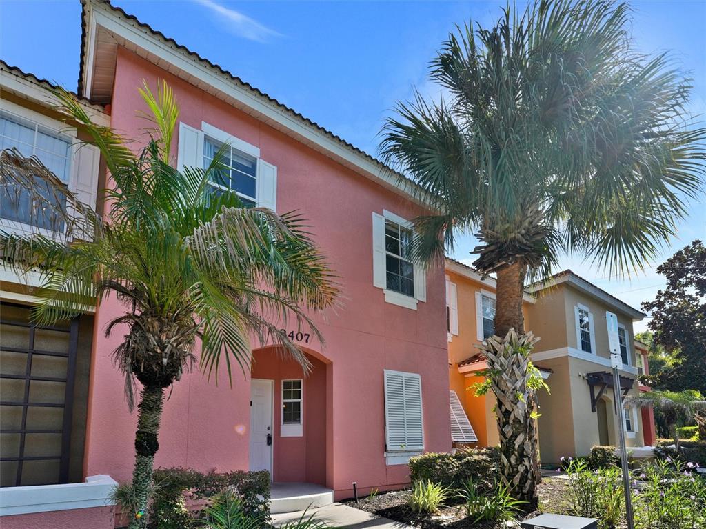 A pink two-story townhouse exterior features palm trees, white shutters, and a recessed entryway — 8407 BLUE LAGOON DRIVE, KISSIMMEE, FL