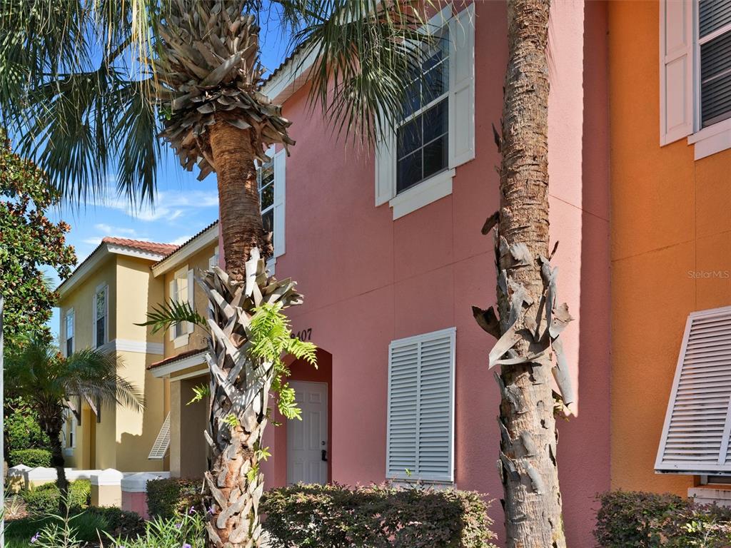 A pink two-story townhouse exterior features palm trees, white shutters, and a front entrance — 8407 BLUE LAGOON DRIVE, KISSIMMEE, FL