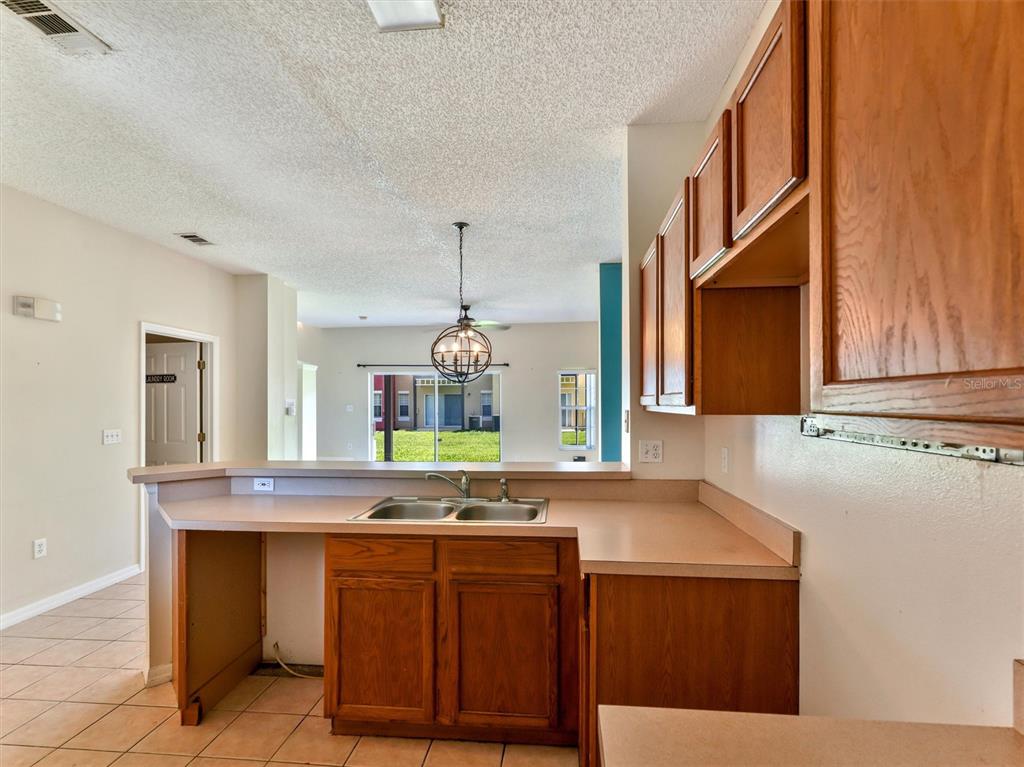 A kitchen features wood cabinets, laminate countertops, a double sink, and an open floor plan — 8407 BLUE LAGOON DRIVE, KISSIMMEE, FL