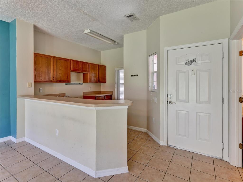 A kitchen with wood cabinets and a breakfast bar overlooks a tiled entryway — 8407 BLUE LAGOON DRIVE, KISSIMMEE, FL