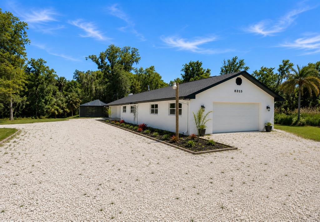 A white brick house with a garage and a gravel driveway under a blue sky — 8315 REVELS ROAD, RIVERVIEW, FL