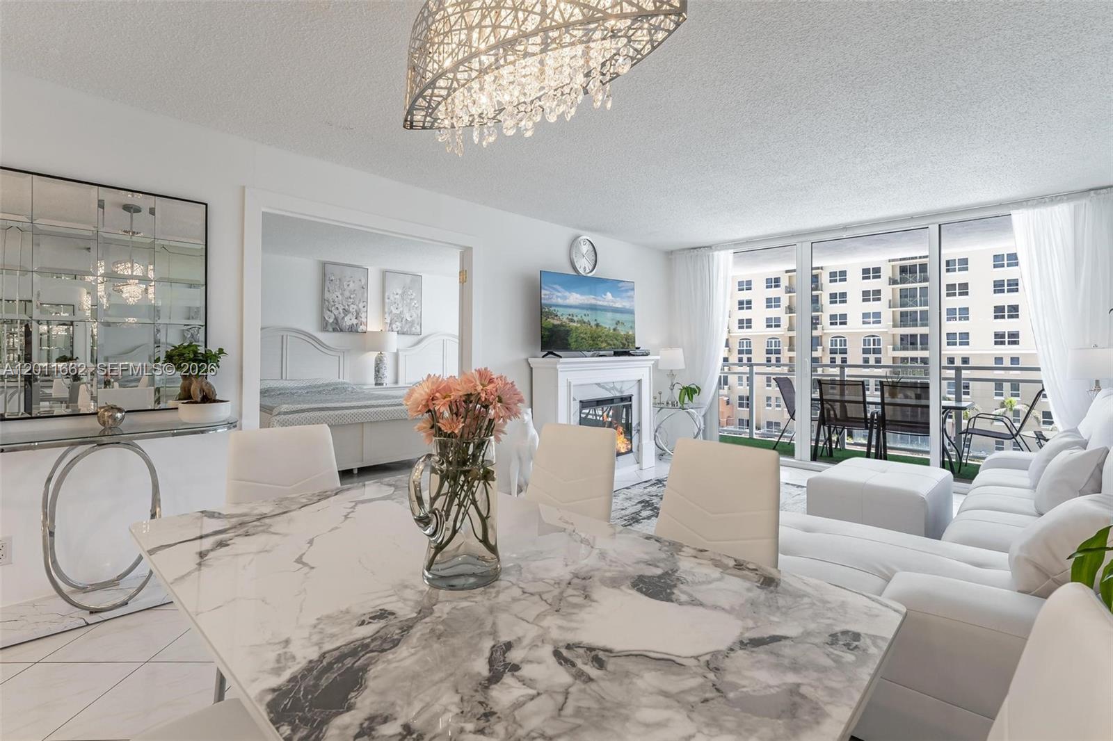 A bright living and dining area features a marble table, white furniture, and a balcony — HALLANDALE BEACH, FL