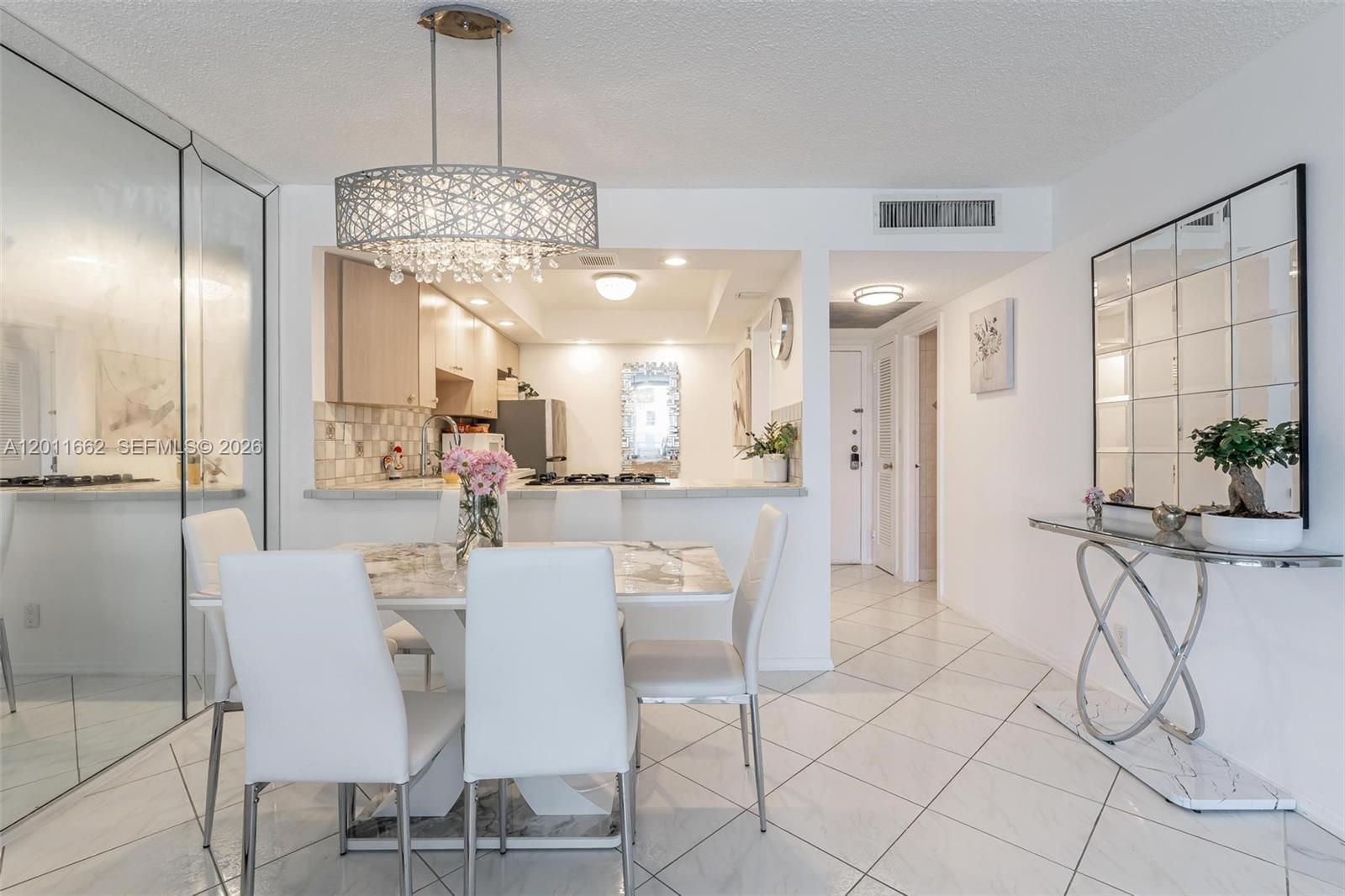 A dining area with a marble table, white chairs, and a chandelier, adjacent to a kitchen — HALLANDALE BEACH, FL