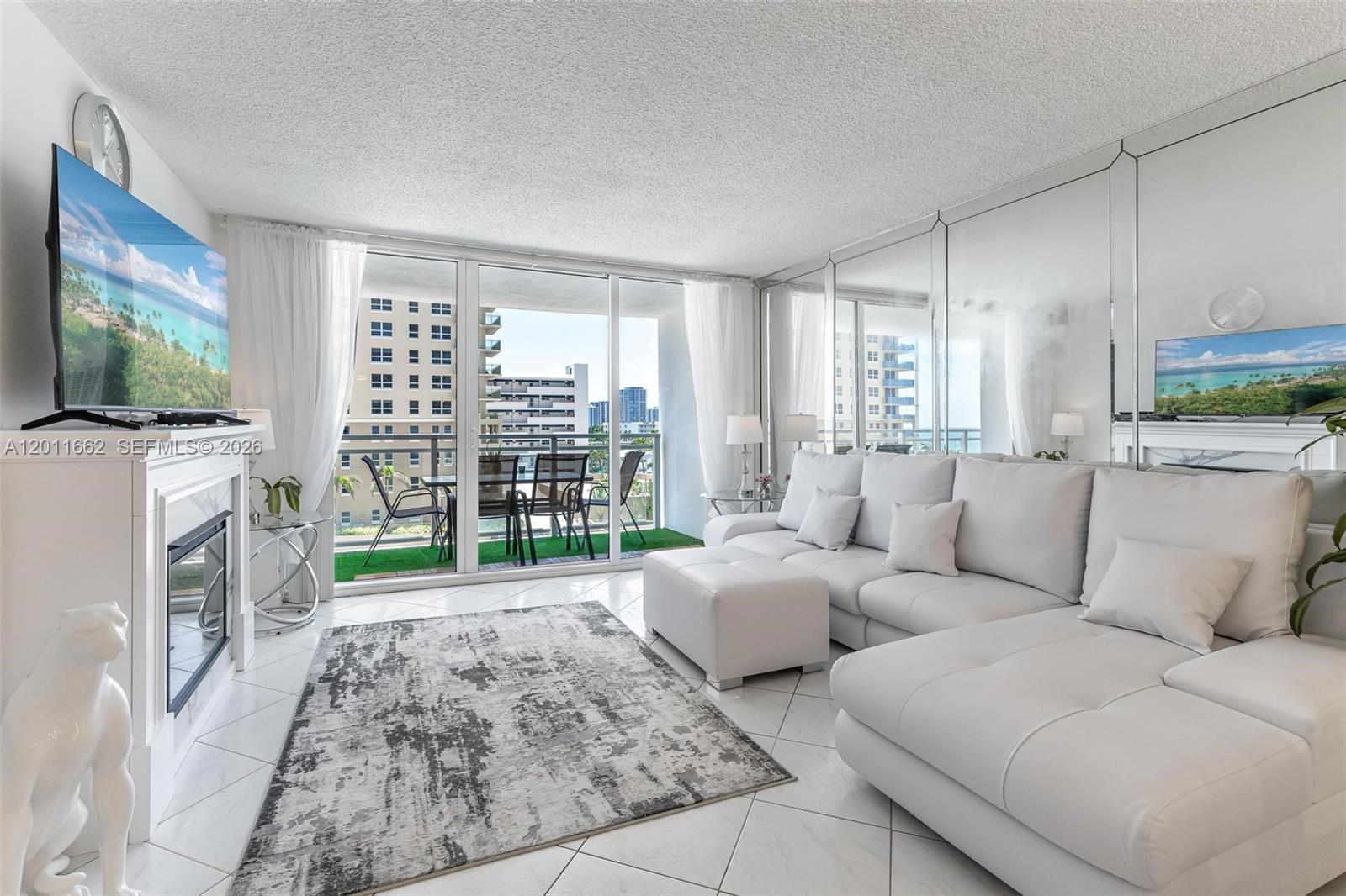 A living room features a white sectional sofa, a fireplace, and a balcony with seating — HALLANDALE BEACH, FL