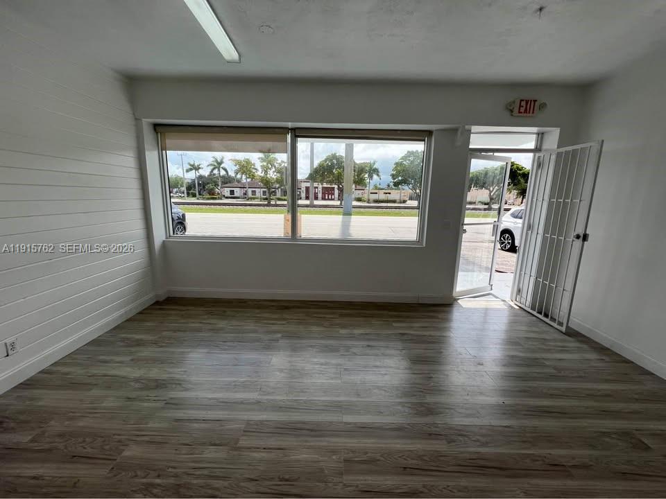 An empty room features wood-look flooring, white walls, large windows, and an open security door — 1812 N Dixie Hwy, Hollywood FL 33020, HOLLYWOOD, FL