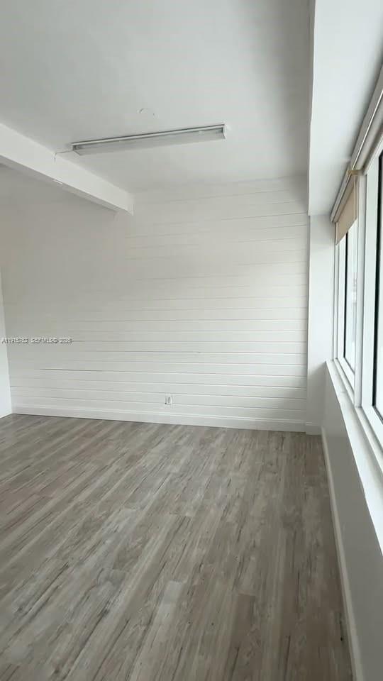 An empty room features light wood-look flooring, white shiplap walls, and a large window — 1812 N Dixie Hwy, Hollywood FL 33020, HOLLYWOOD, FL