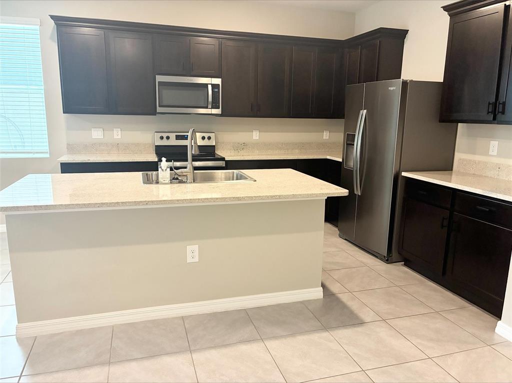A kitchen features dark wood cabinets, stainless steel appliances, a granite island, and tile flooring — 2908 EVERGREEN ELM PASS, WESLEY CHAPEL, FL