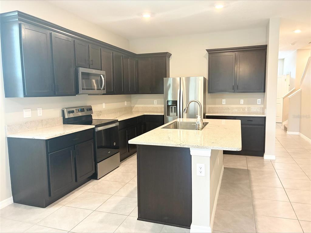 A kitchen features dark wood cabinets, light granite countertops, stainless steel appliances, and a central island — 2908 EVERGREEN ELM PASS, WESLEY CHAPEL, FL