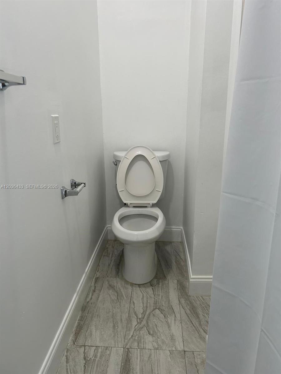 A white toilet is positioned in a small bathroom with light-colored tile flooring — 16271 SW 92nd Ter # 0, Miami FL 33196, MIAMI, FL