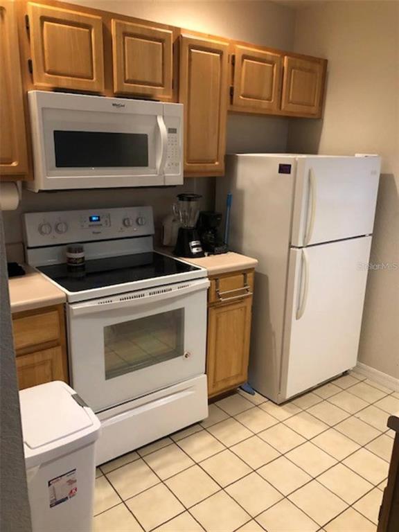 A kitchen features light wood cabinets, white appliances, and a tiled floor — 4006 VENETIAN BAY DRIVE UNIT 108, KISSIMMEE, FL