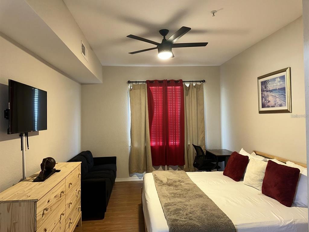 A bedroom features a bed, a black sofa, a wooden dresser, and a ceiling fan — 4006 VENETIAN BAY DRIVE UNIT 108, KISSIMMEE, FL