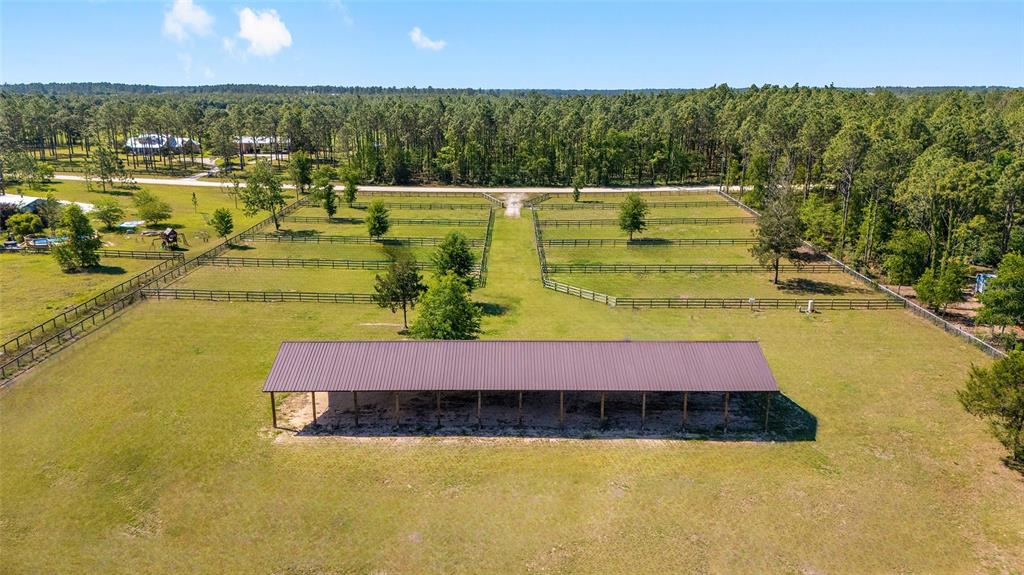 An aerial view shows a long, open-sided metal shed situated in a fenced pasture — 13531 SE 54TH STREET, MORRISTON, FL