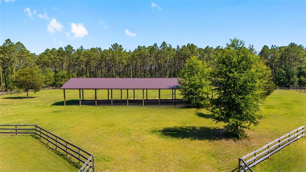 An open-sided metal pole barn stands in a grassy field enclosed by wooden fencing — 13531 SE 54TH STREET, MORRISTON, FL