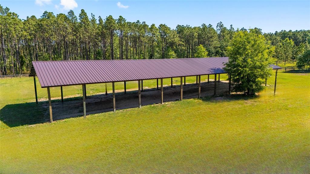 An aerial view of a long, open-sided metal pole barn situated in a grassy field — 13531 SE 54TH STREET, MORRISTON, FL