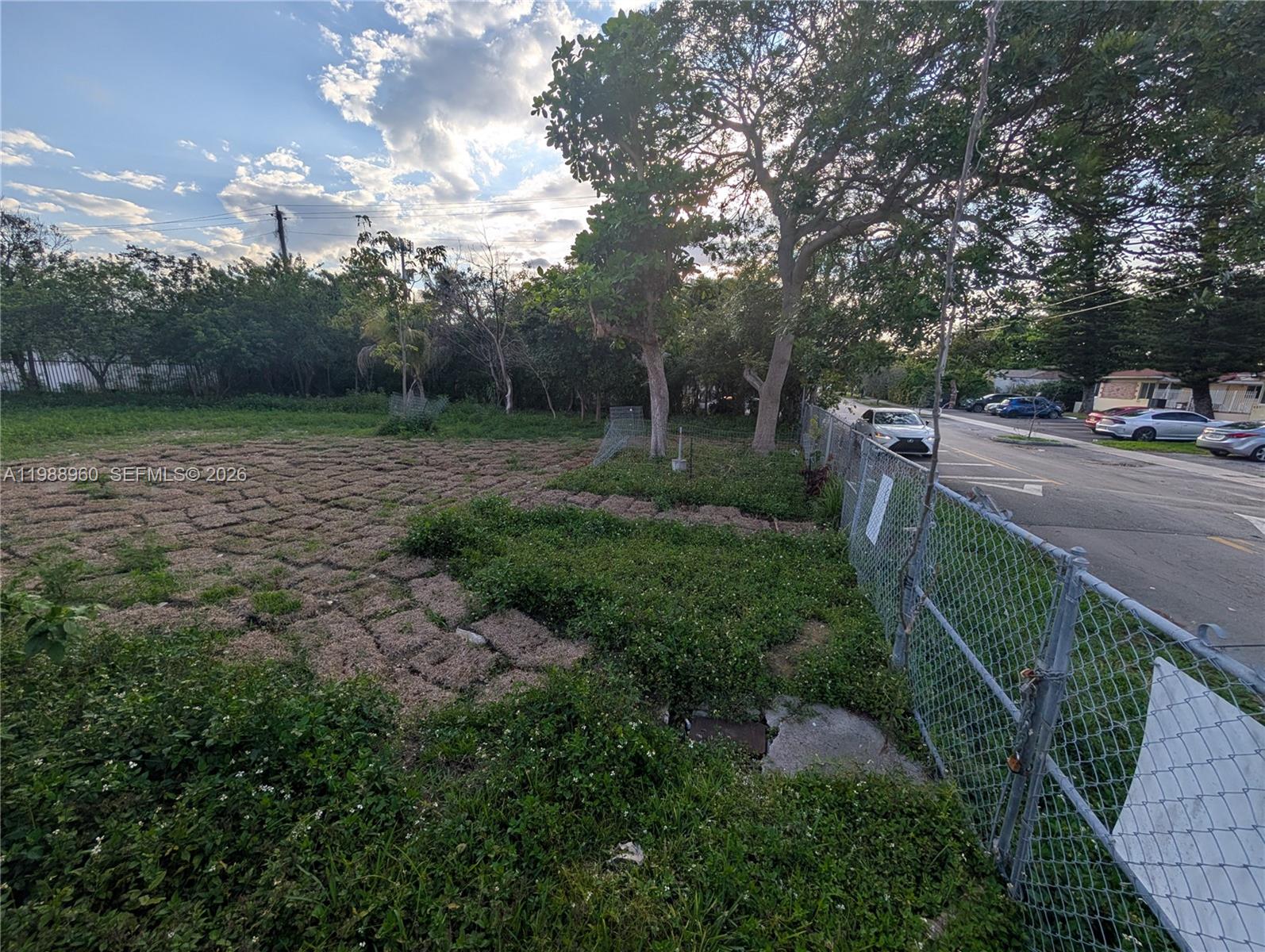 A fenced, vacant lot features patches of dry ground and green vegetation near a paved road — 660 NE 86th St, Miami FL 33138, MIAMI, FL