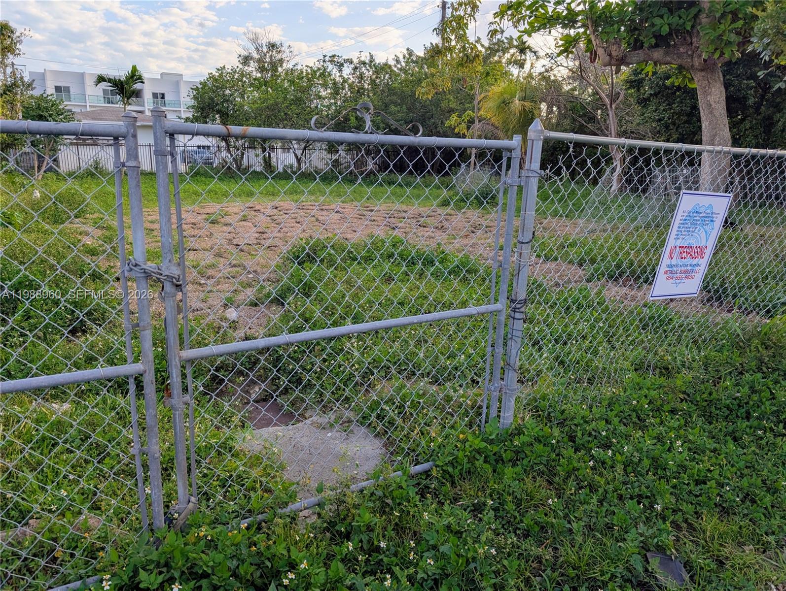 A chain-link fence encloses a vacant, grassy lot with a no trespassing sign attached — 660 NE 86th St, Miami FL 33138, MIAMI, FL