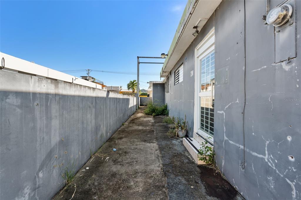 A narrow concrete walkway runs between a gray exterior wall and a tall concrete fence — #2 CALLE PADRE RIVERA WEST, HUMACAO, PR