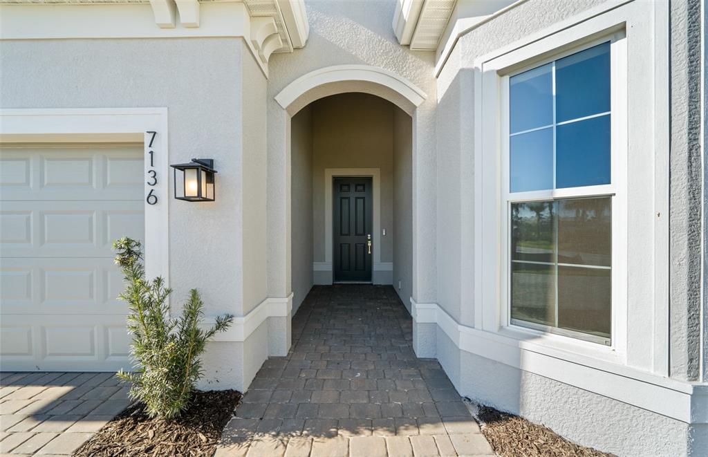 The exterior of a house features a paved walkway leading to a dark front door — 7621 FULHAM AVENUE, BRADENTON, FL