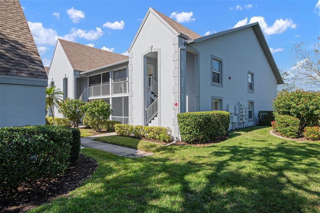 A two-story apartment building with a screened balcony, exterior staircase, and landscaped lawn — 6609 STONE RIVER ROAD UNIT 206, BRADENTON, FL