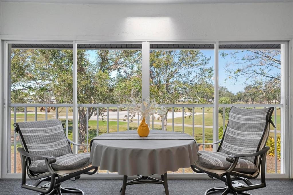A screened-in balcony features a round table with two chairs overlooking a golf course — 6609 STONE RIVER ROAD UNIT 206, BRADENTON, FL