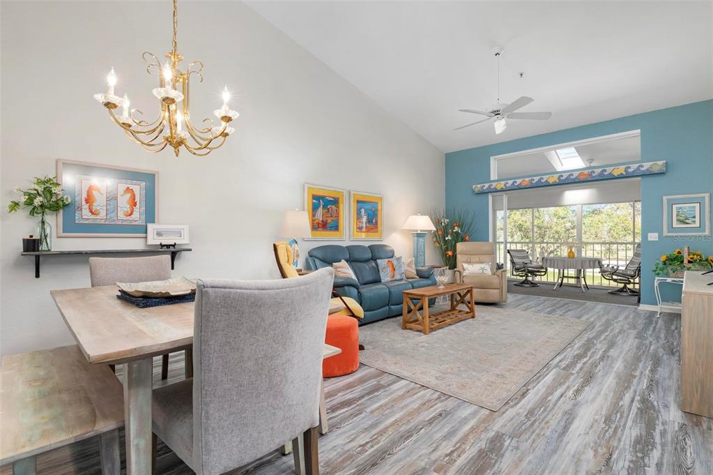A living and dining area features vaulted ceilings, wood-look flooring, and a blue accent wall — 6609 STONE RIVER ROAD UNIT 206, BRADENTON, FL