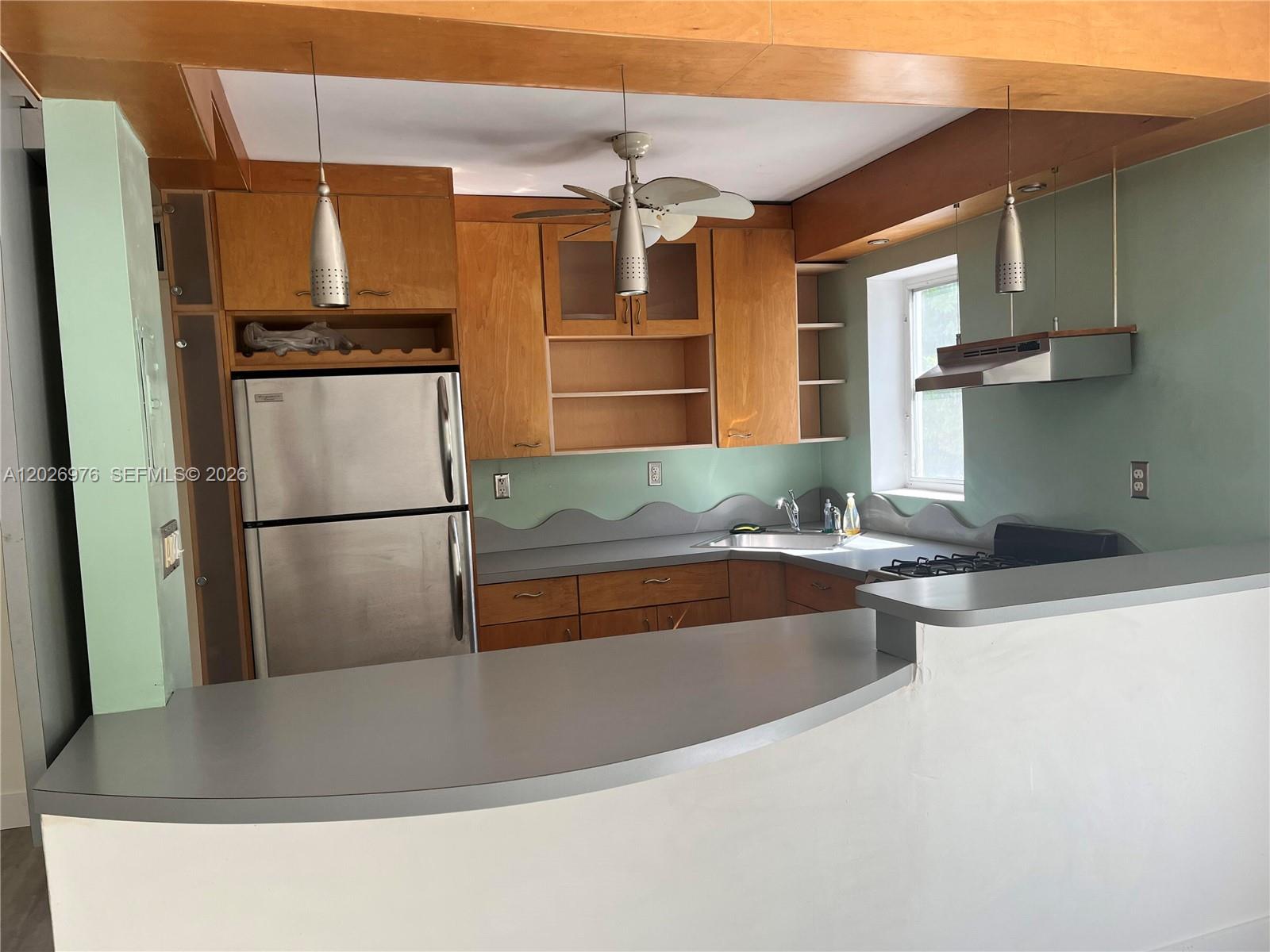 A kitchen features wood cabinets, a gray countertop, stainless steel appliances, and a breakfast bar — 240 Collins Ave # 2B, Miami Beach FL 33139, MIAMI BEACH, FL