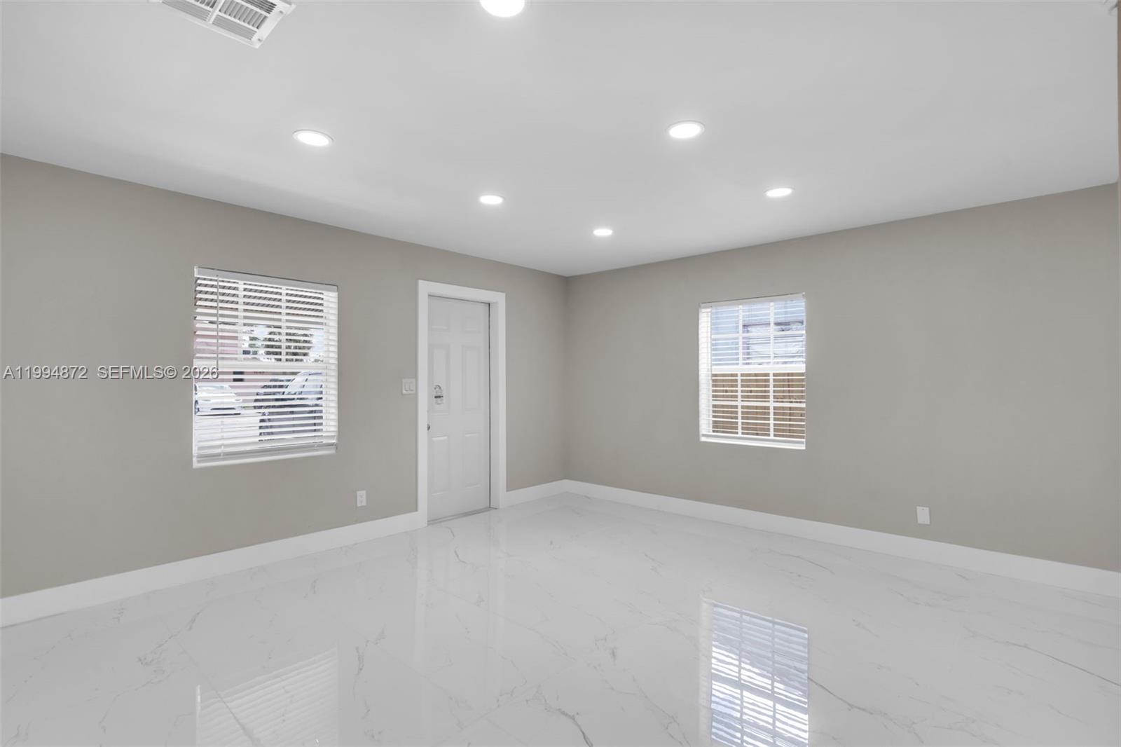 An empty room features light gray walls, white tile flooring, recessed lighting, and two windows — 1660 W 26th St, Riviera Beach FL 33404, RIVIERA BEACH, FL