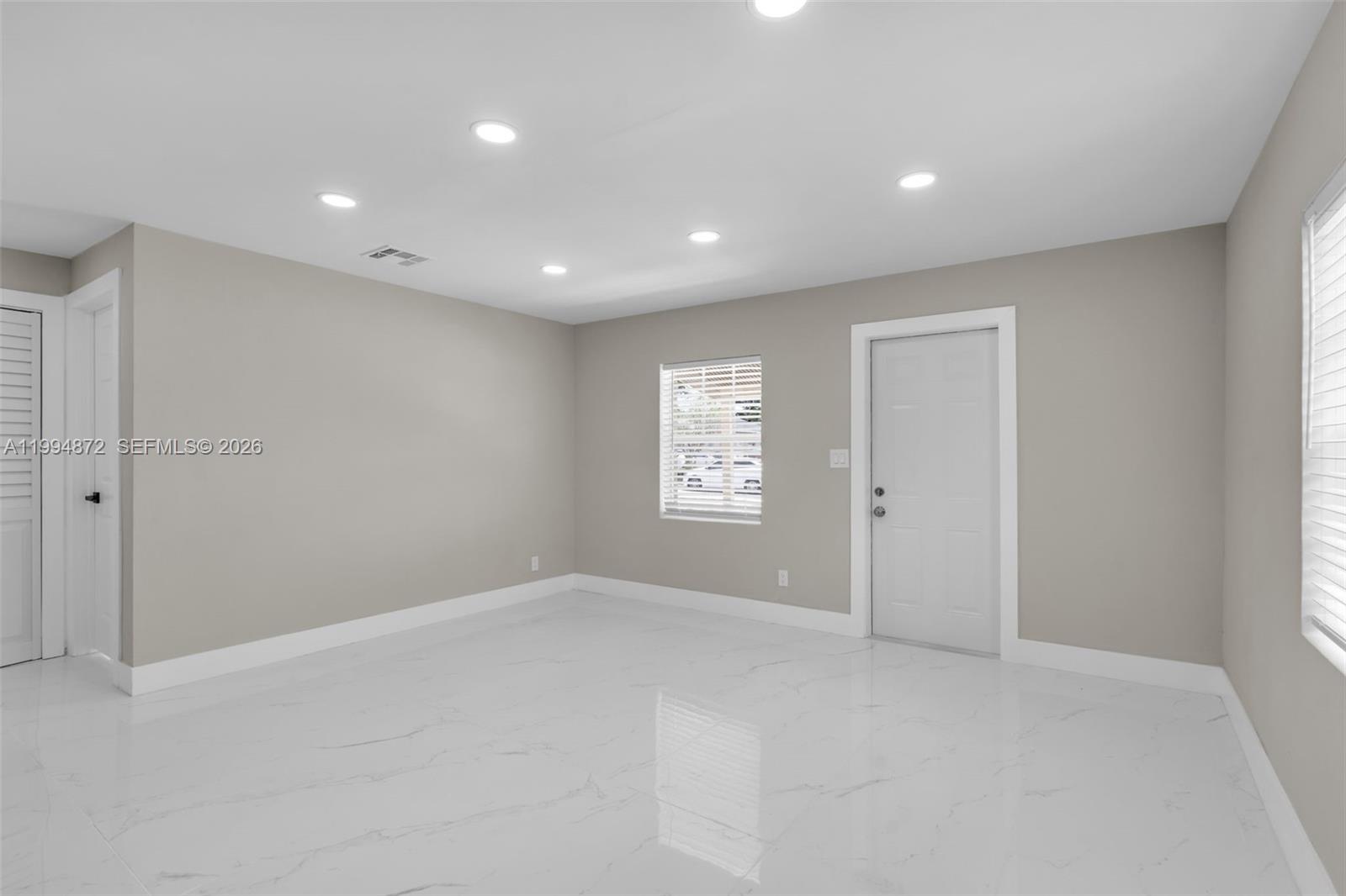 An empty room features light gray walls, white tile flooring, recessed lighting, and two doors — 1660 W 26th St, Riviera Beach FL 33404, RIVIERA BEACH, FL