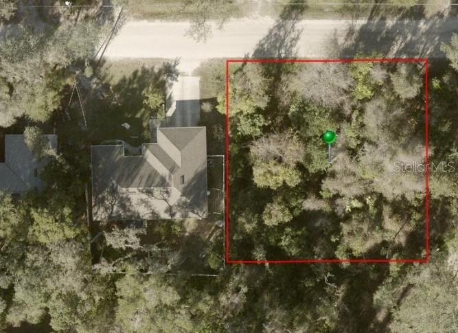 This aerial view shows a wooded vacant lot outlined in red next to a house — 1424 10TH STREET, ORANGE CITY, FL