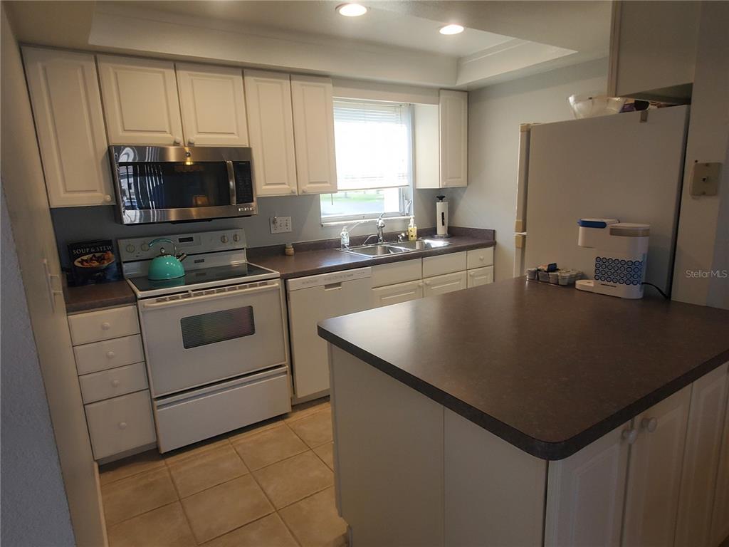 A kitchen features white cabinets, dark countertops, a stainless steel microwave, and a white stove — 311 GARVIN STREET UNIT 407A, PUNTA GORDA, FL