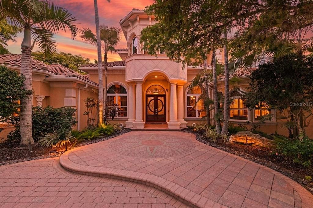 A Mediterranean-style house exterior features a paved circular driveway, arched windows, and palm trees — 7202 TEAL CREEK GLEN, LAKEWOOD RANCH, FL