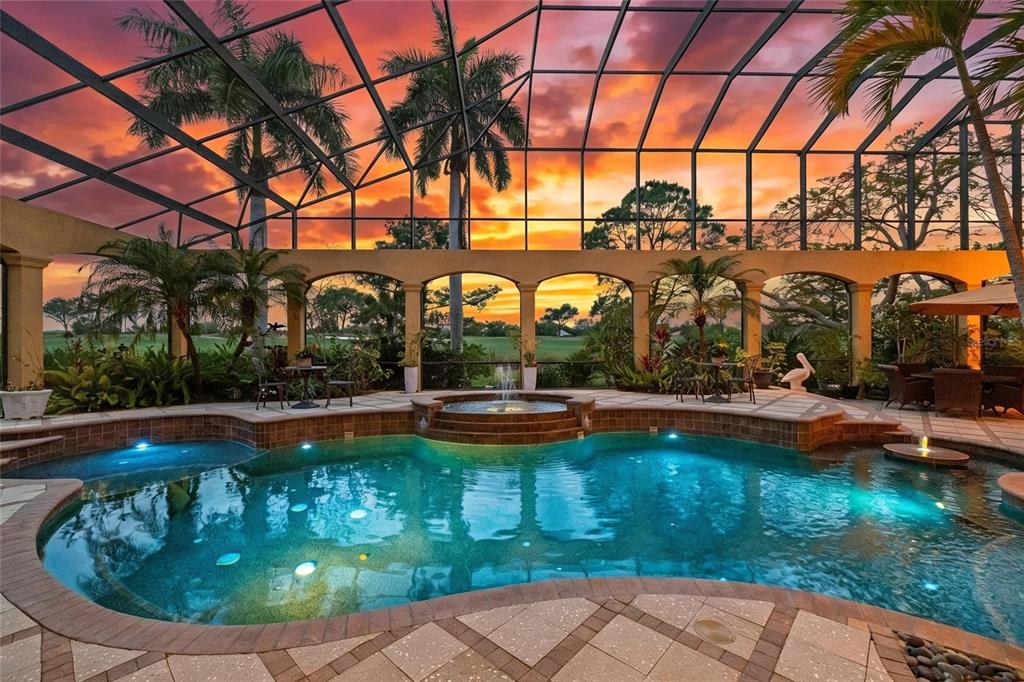 A screened-in swimming pool with a spa and fountain overlooks a golf course at sunset — 7202 TEAL CREEK GLEN, LAKEWOOD RANCH, FL