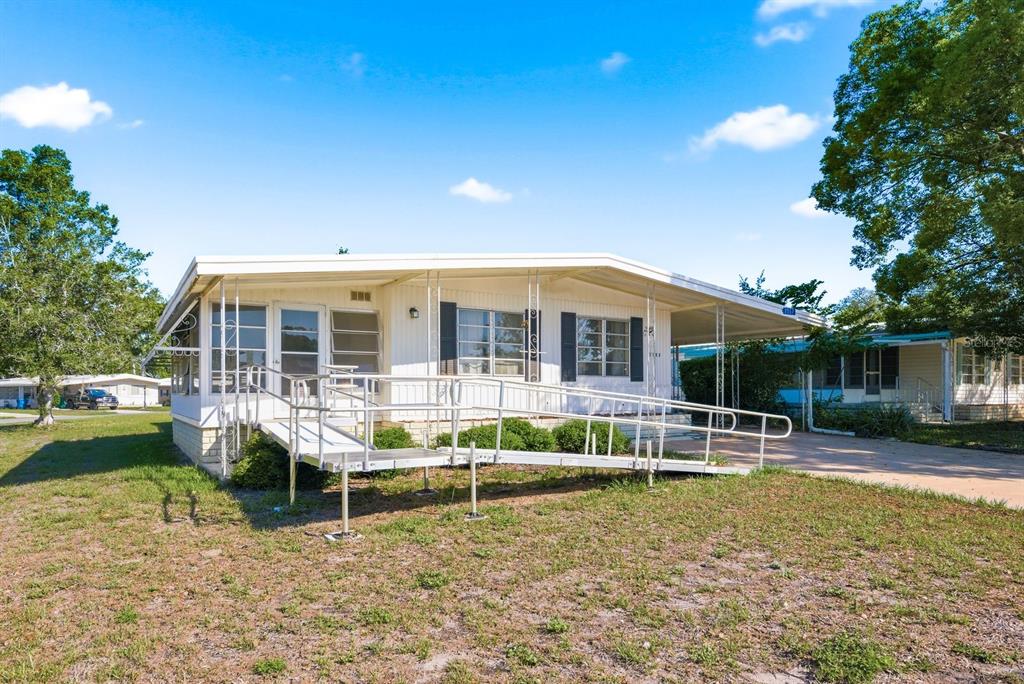 A single-story manufactured home features a metal wheelchair ramp and a covered carport — 7557 FAIRLANE AVENUE, BROOKSVILLE, FL