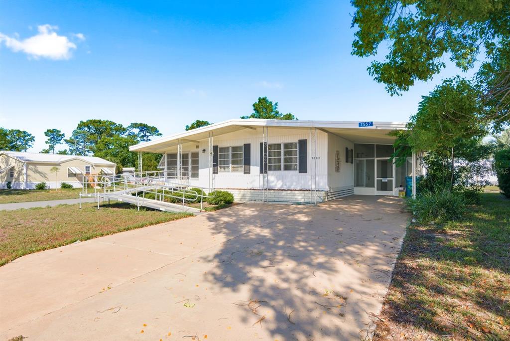 A single-story manufactured home features a concrete driveway, a wheelchair ramp, and a carport — 7557 FAIRLANE AVENUE, BROOKSVILLE, FL